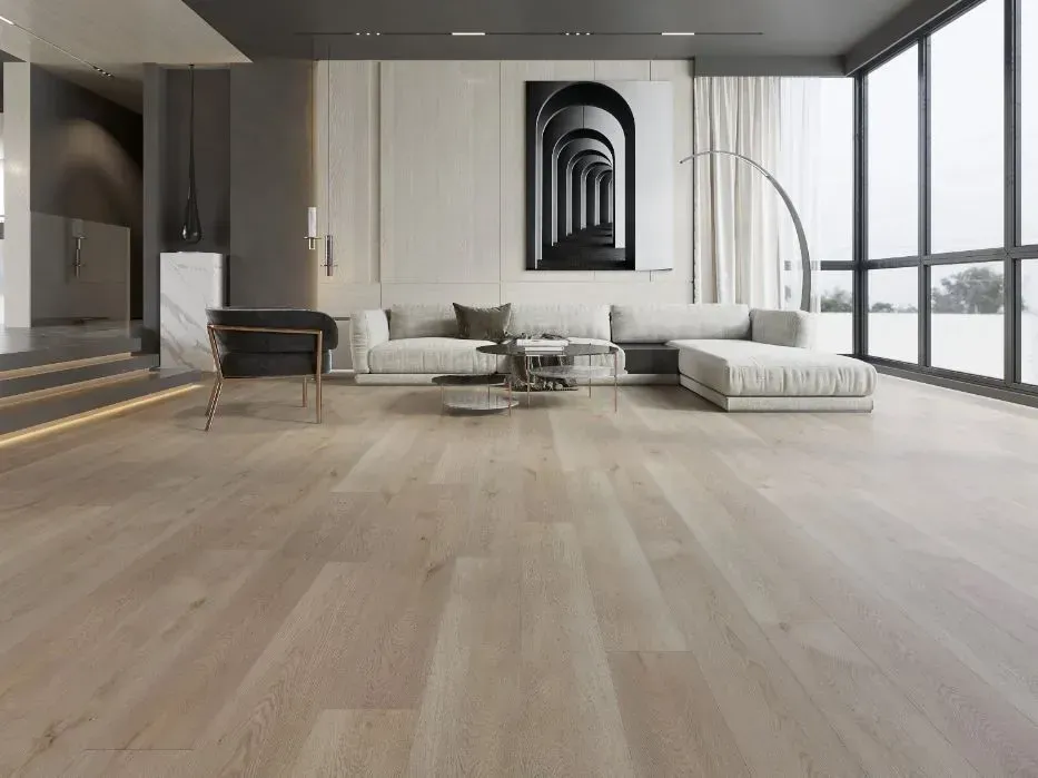 A modern, minimalist living room with light oak flooring, a white sectional sofa, a black accent chair, and wall art.