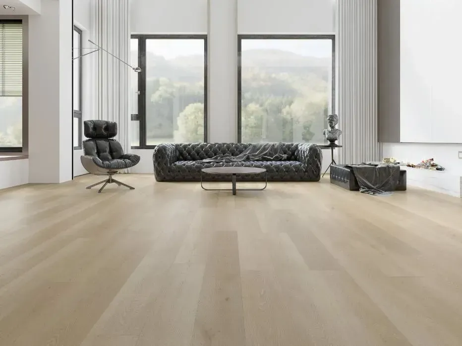 A modern living room with light wood floors, a black leather tufted sofa, and an armchair facing large windows.