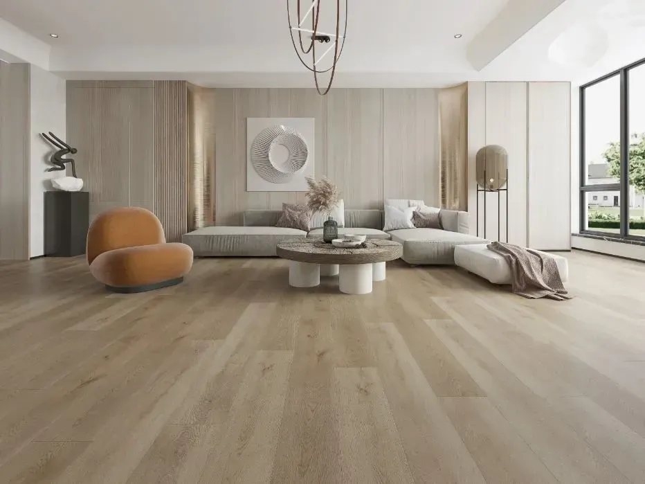 A bright, modern living room with light wood floors, a neutral sectional sofa, a round coffee table, and an orange chair.