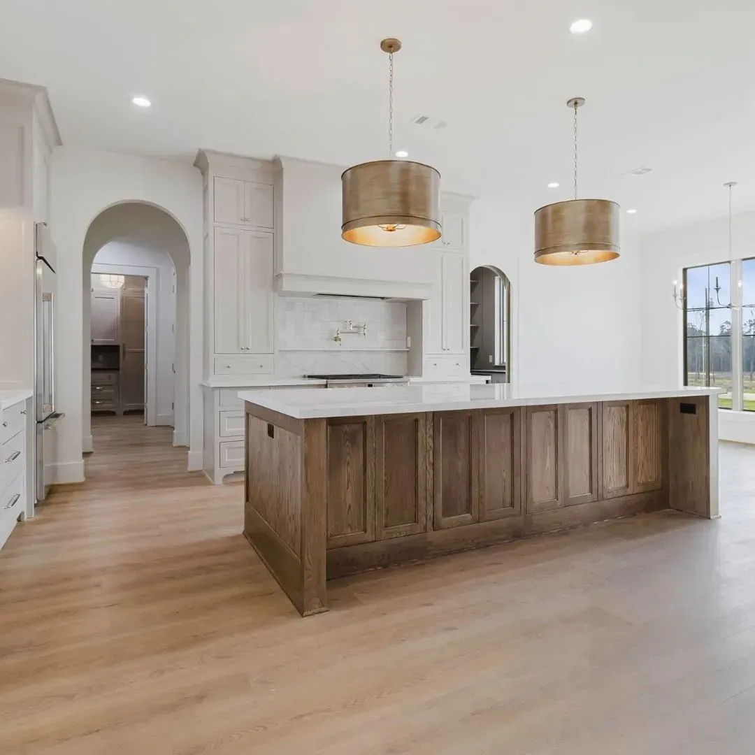 A bright kitchen with light wooden floors, a large wooden island with a white countertop, and two bronze pendant lights.