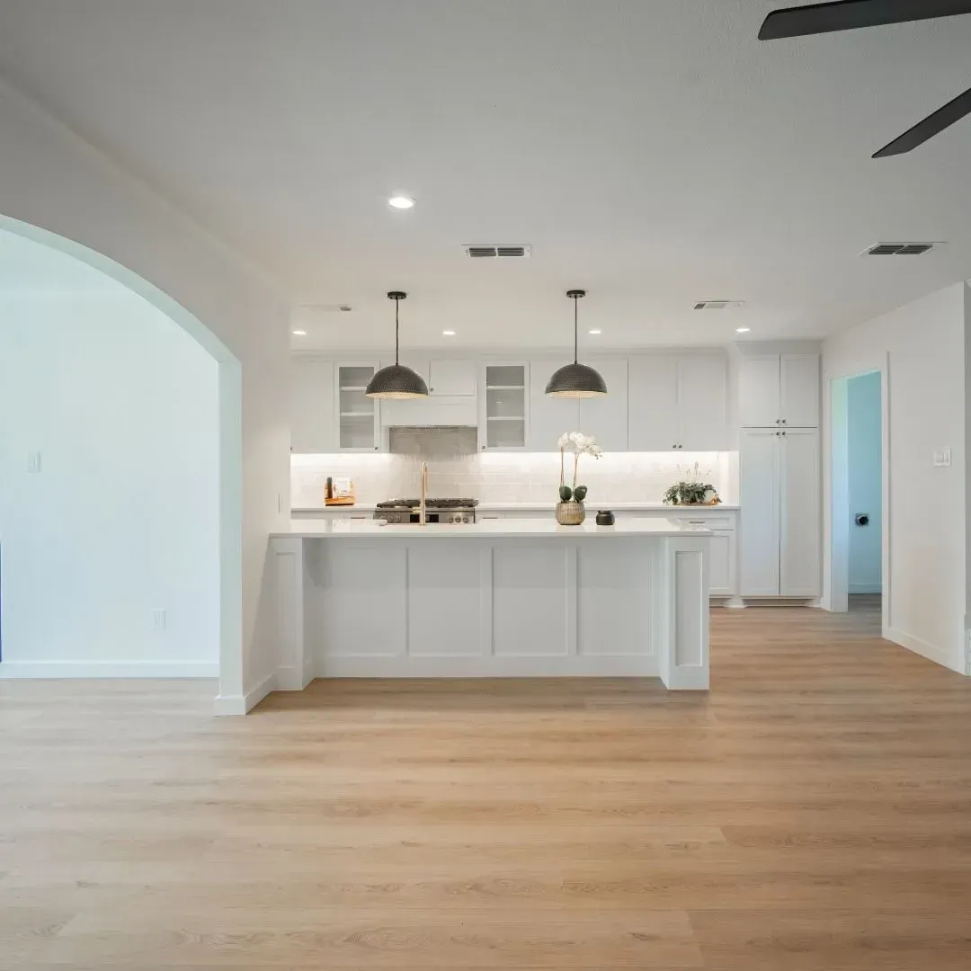 A bright, modern kitchen featuring white cabinets, a large center island, pendant lights, and light wood flooring.