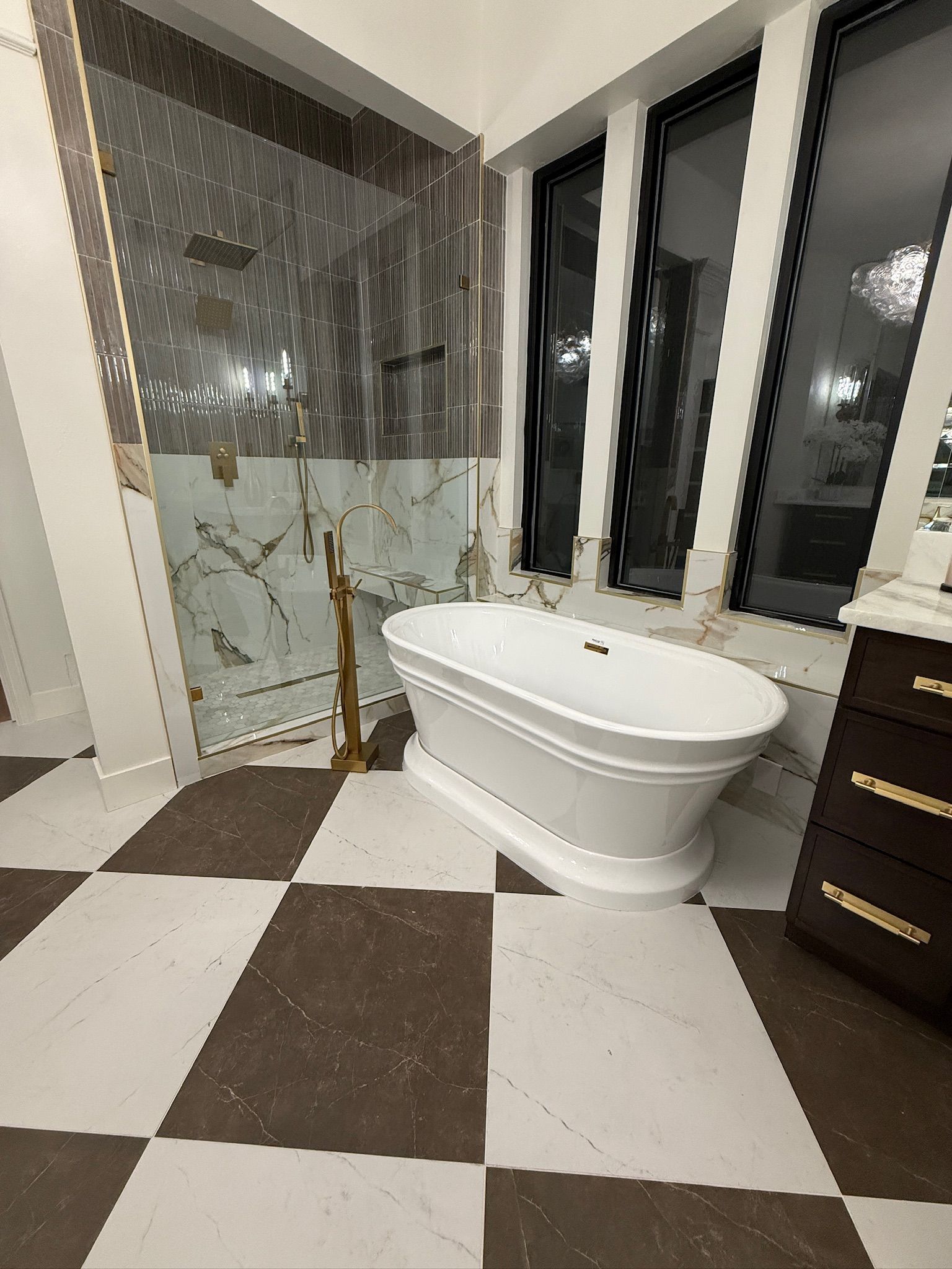 A modern bathroom featuring a white freestanding tub on a black-and-white checkered floor next to a glass-enclosed shower.