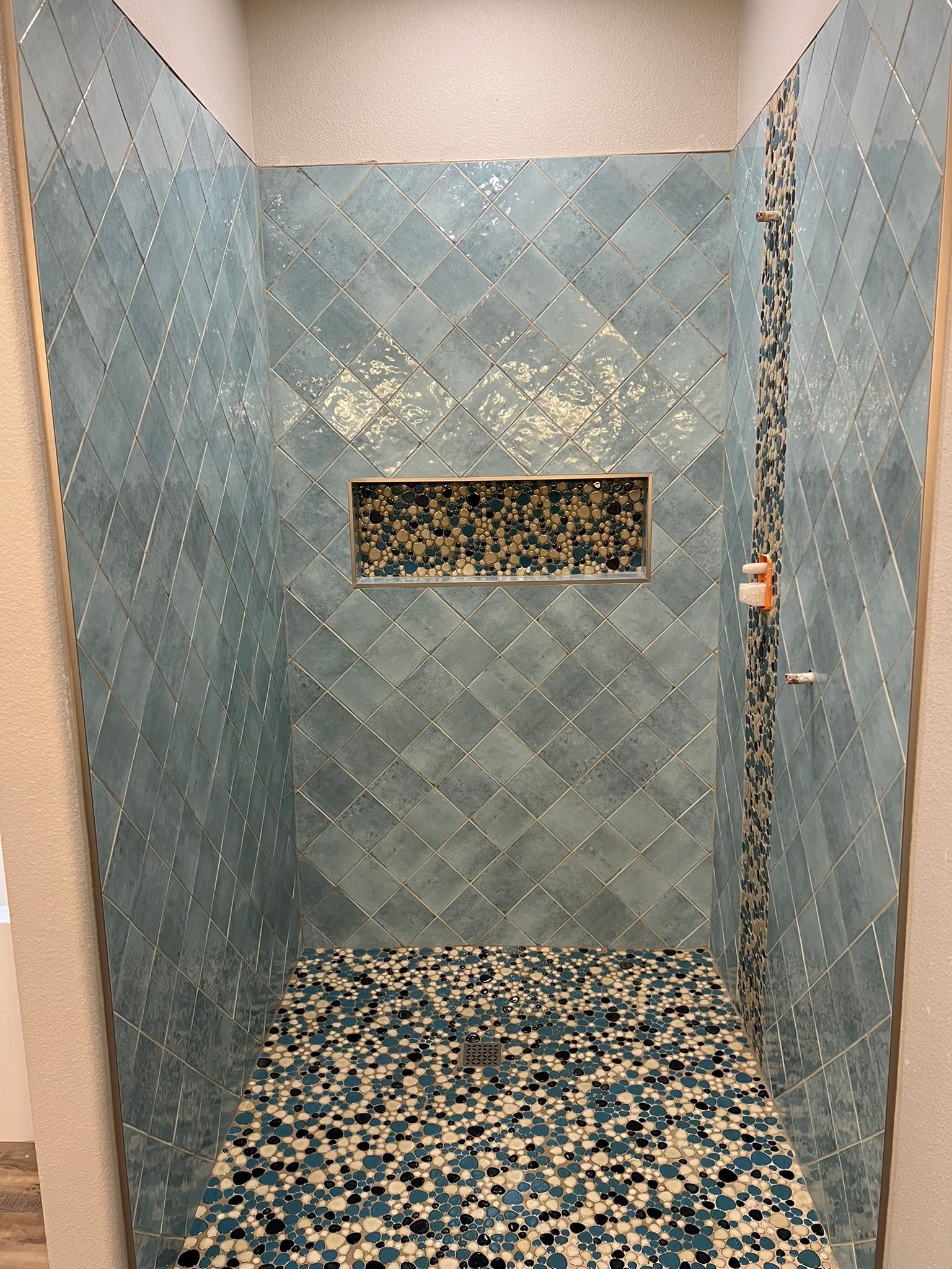 A shower with blue diamond-patterned wall tiles, a mosaic-tiled niche, and a matching pebble-covered floor.