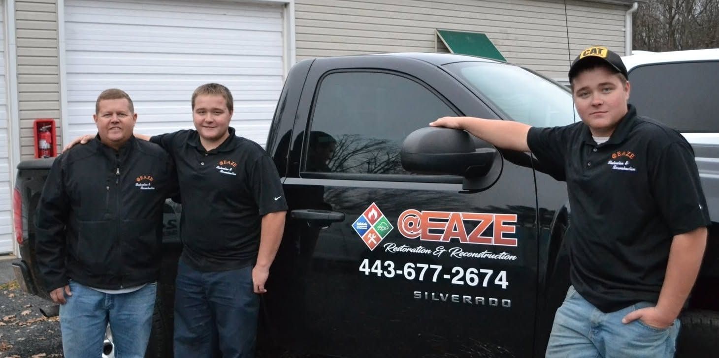 Three people posing beside a black van with a “Craze” logo and phone number