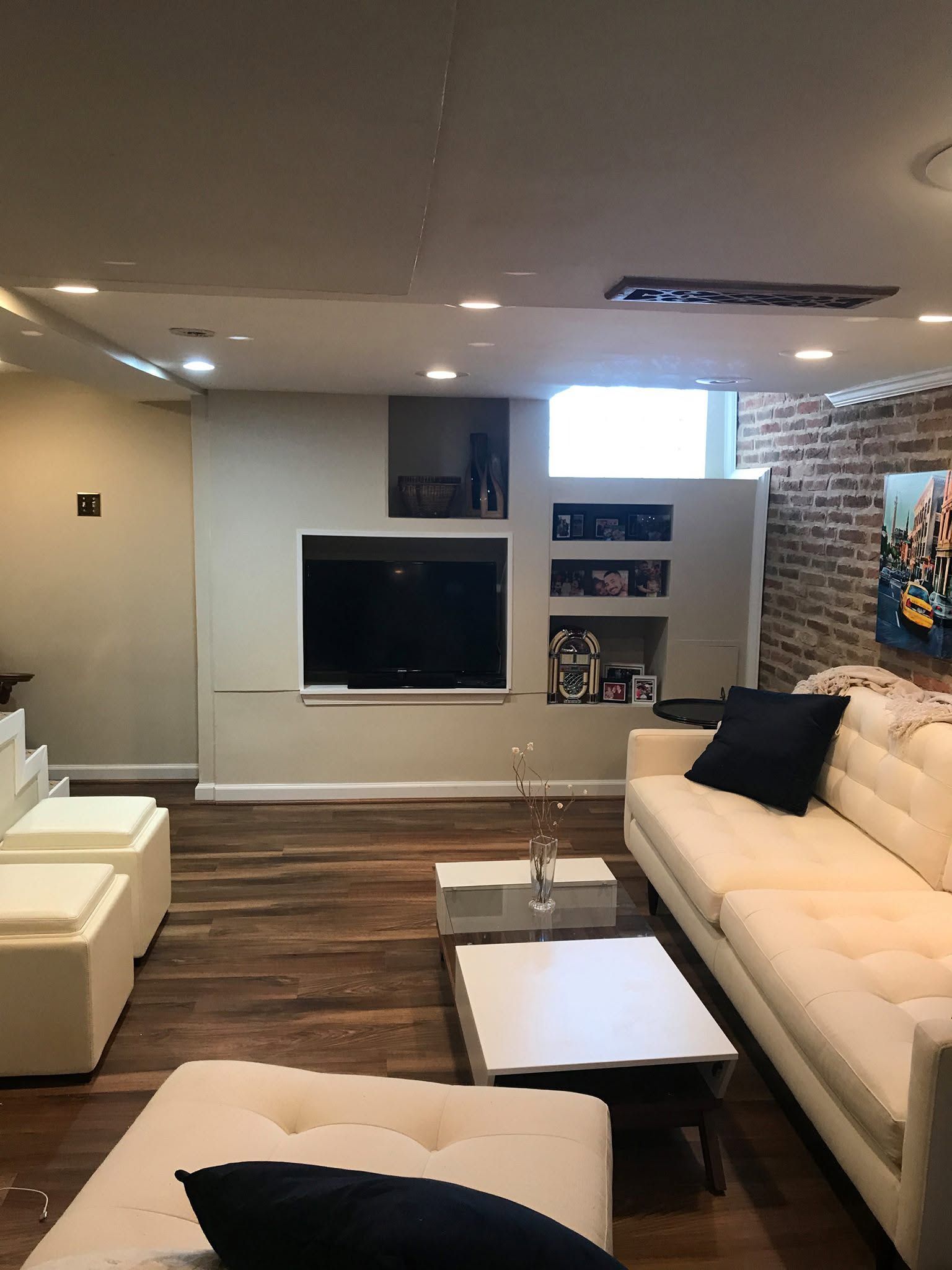 Modern living room with white sofa, ottoman, TV wall, and brick accent wall