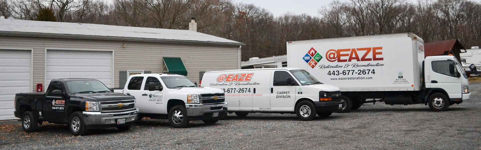 Three work trucks parked in front of a garage, including a white Eaze box truck and pickup trucks.