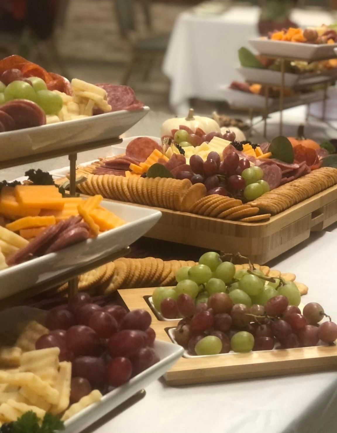 Charcuterie boards with cheese, crackers, grapes, and meats arranged on a tiered serving stand at an event.
