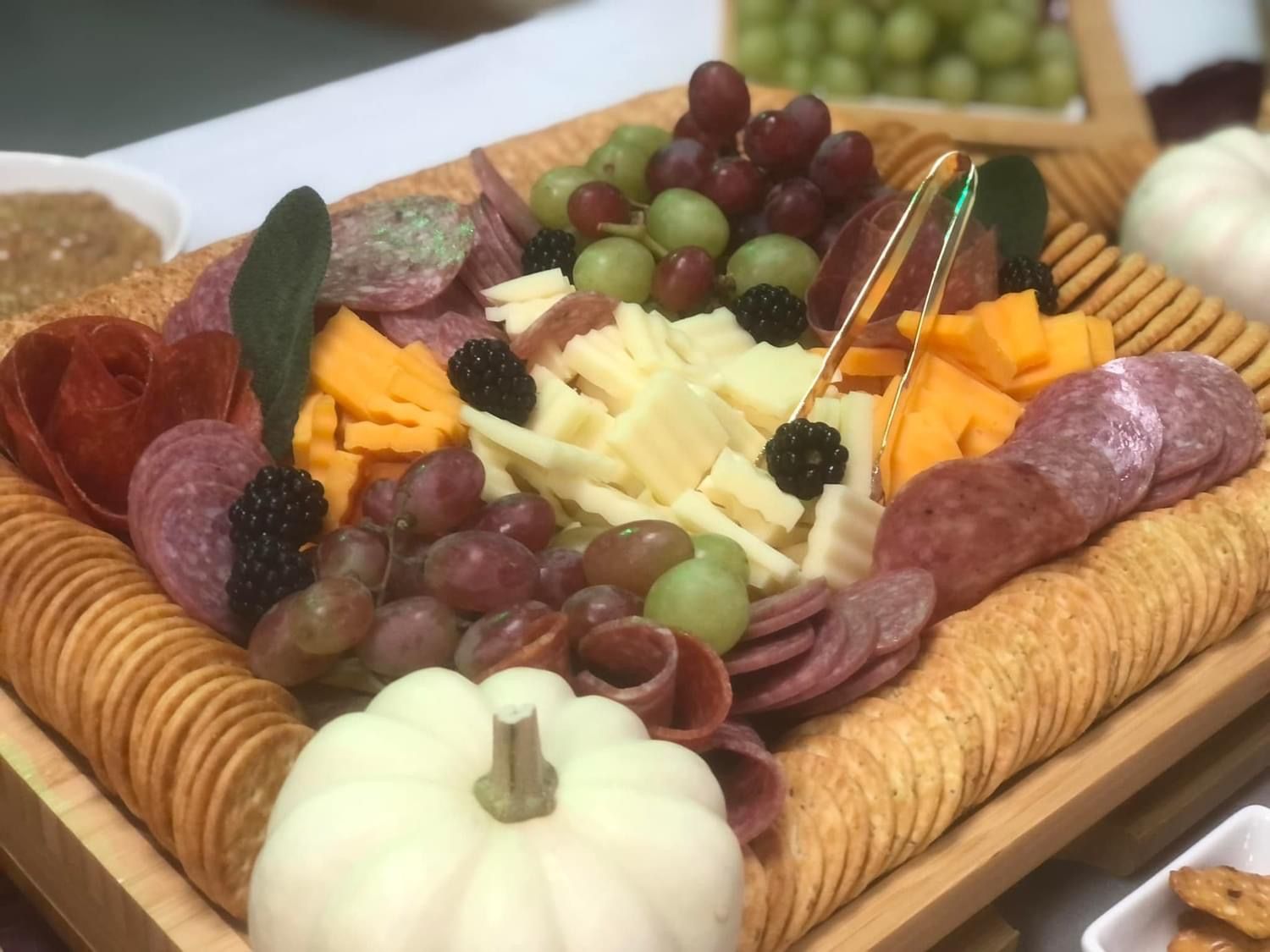 Charcuterie board with cheese, grapes, crackers, and salami. A white pumpkin is in the foreground.