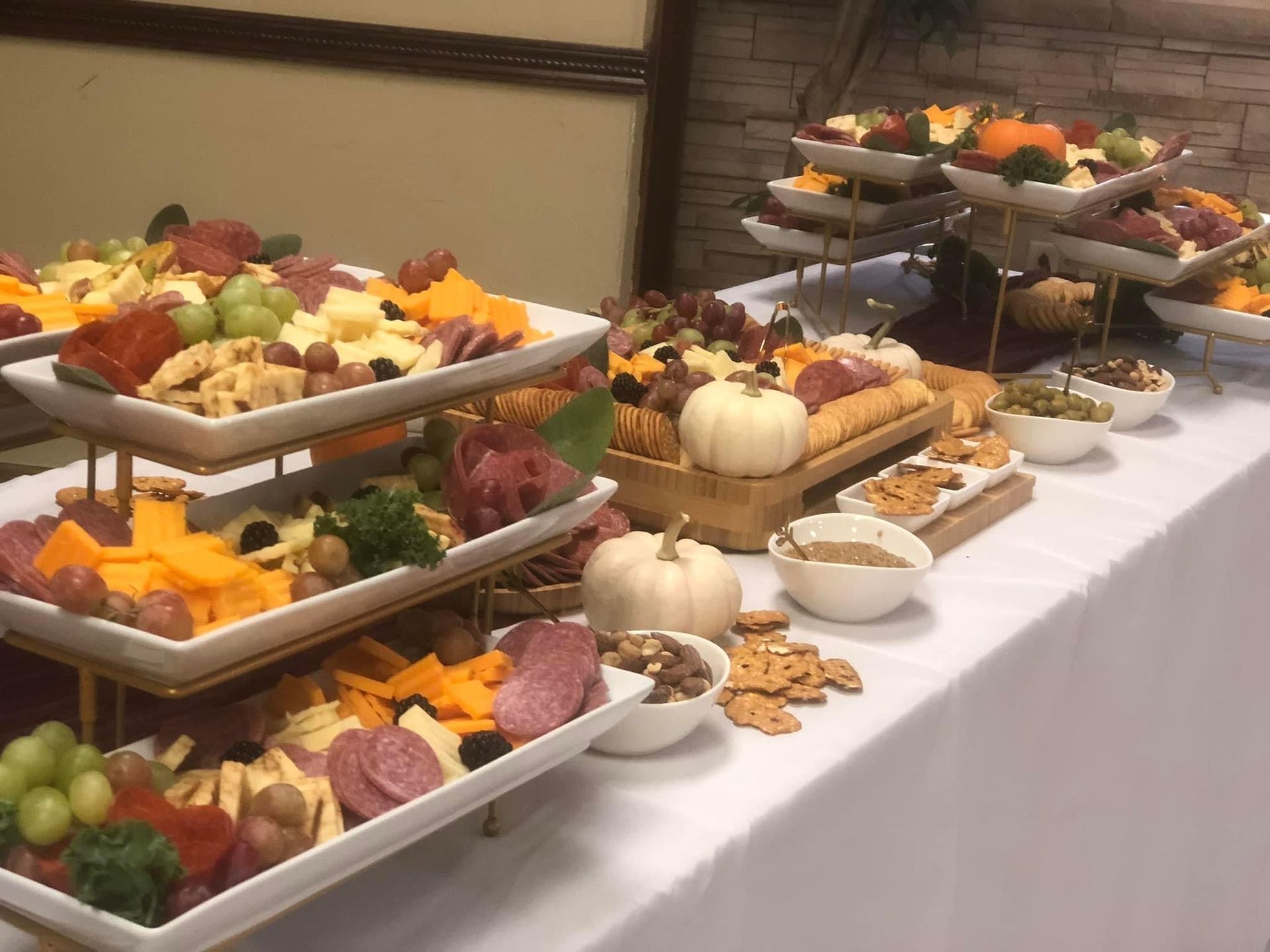 Charcuterie spread: cheeses, meats, crackers, fruits, nuts, and olives on tiered white serving platters on a white-clothed table.