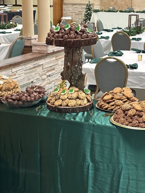 Cookie buffet on a green table. Wooden tree displays cookies, with other platters of treats. Formal dining room setting.