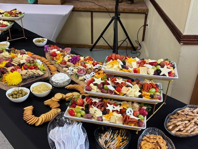 Charcuterie spread on a black-covered table; cheese, crackers, fruit, and dips.