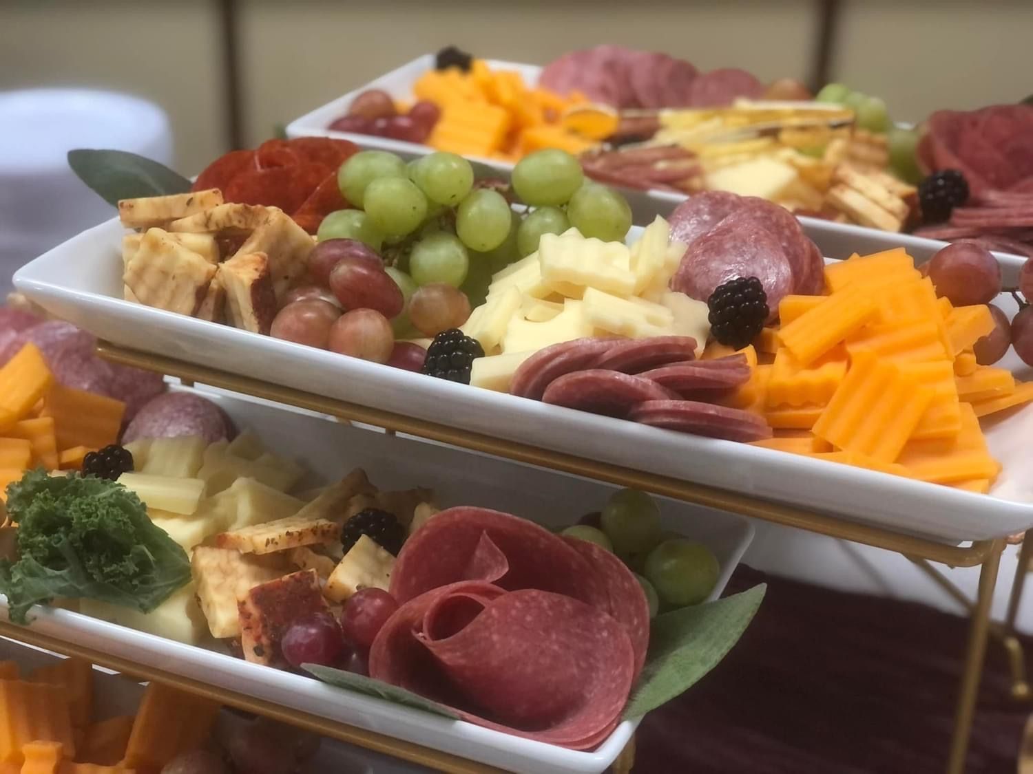 Tiered charcuterie board with meats, cheeses, crackers, and grapes.