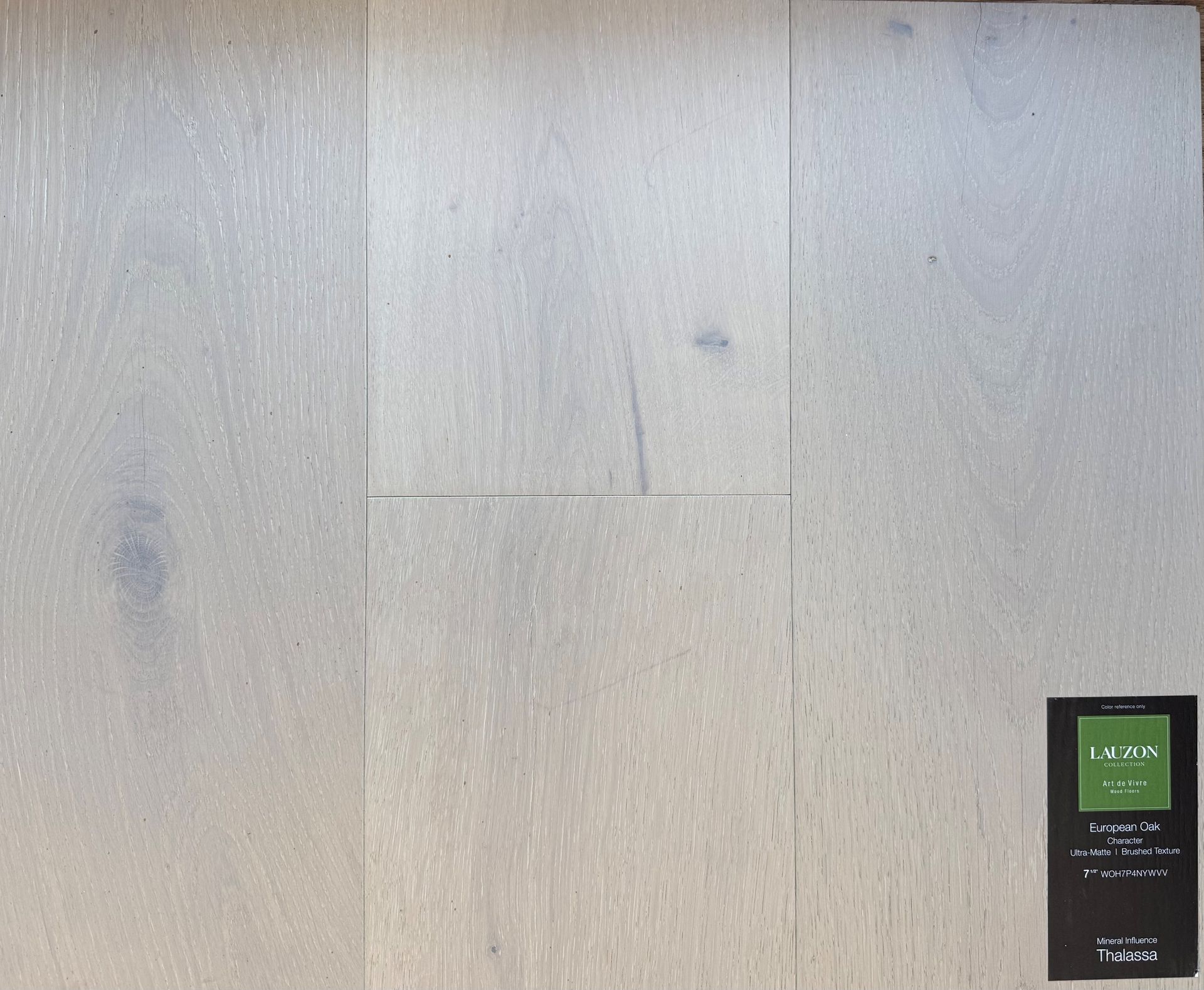 Three light grey wood floor planks laid side-by-side with a product label in the bottom right corner.