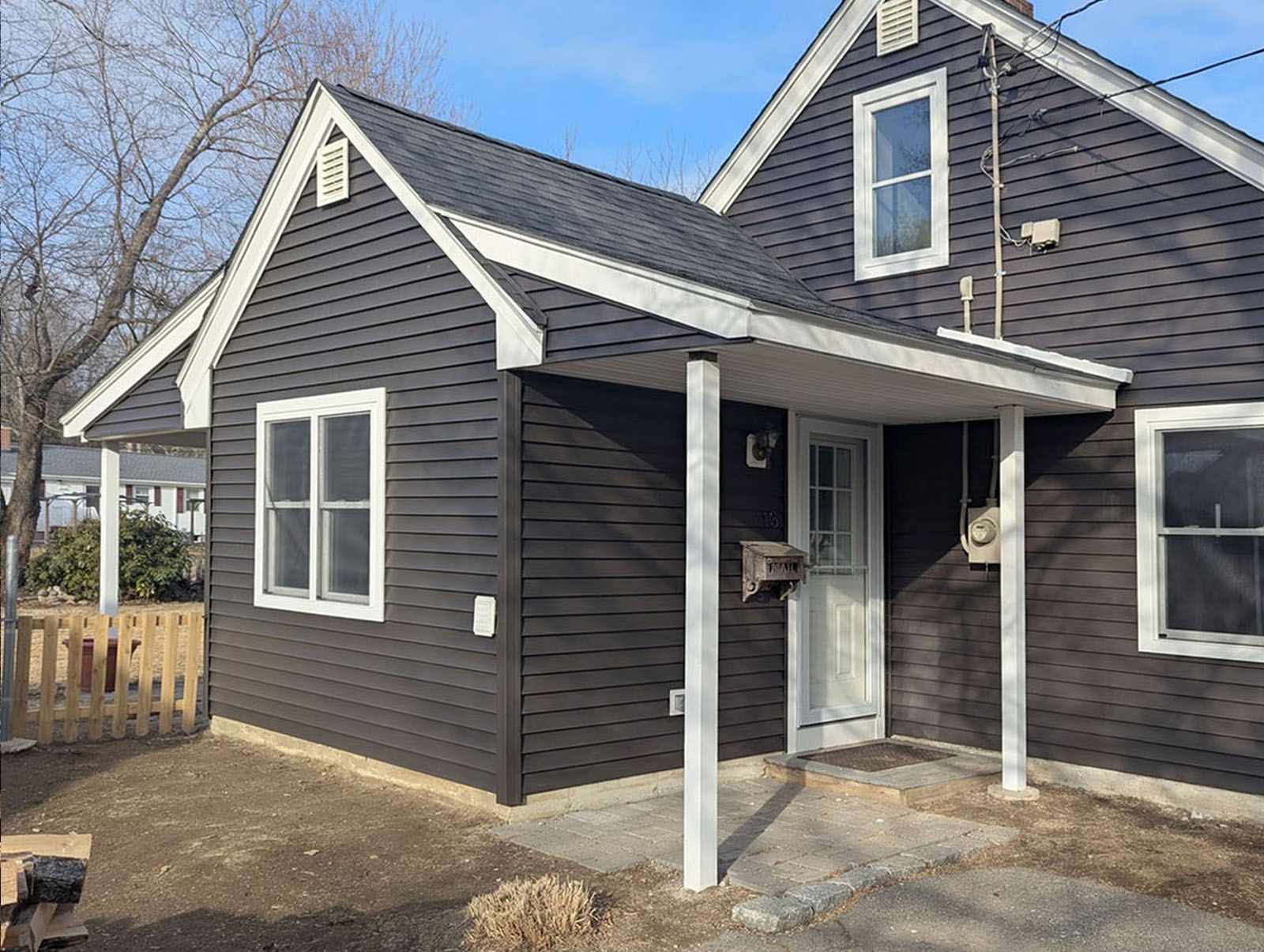 A newly remodeled house exterior with a porch and a fence in front of it