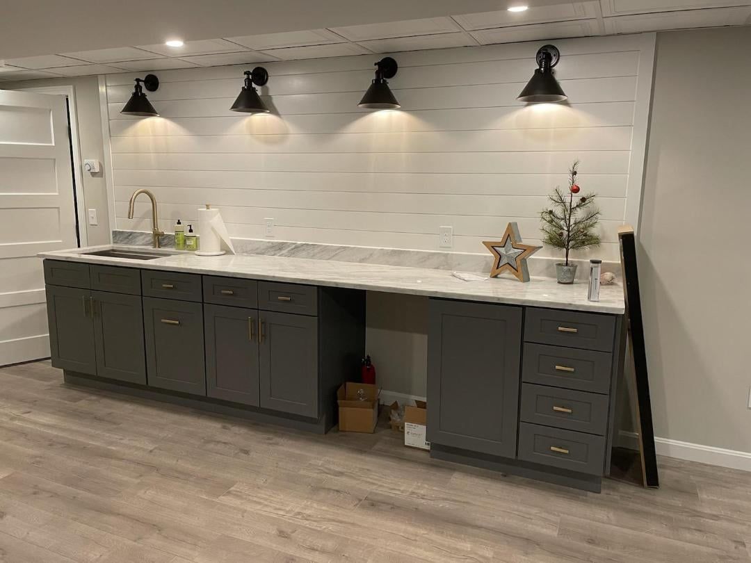 A kitchen with gray cabinets, white countertops, and a sink.