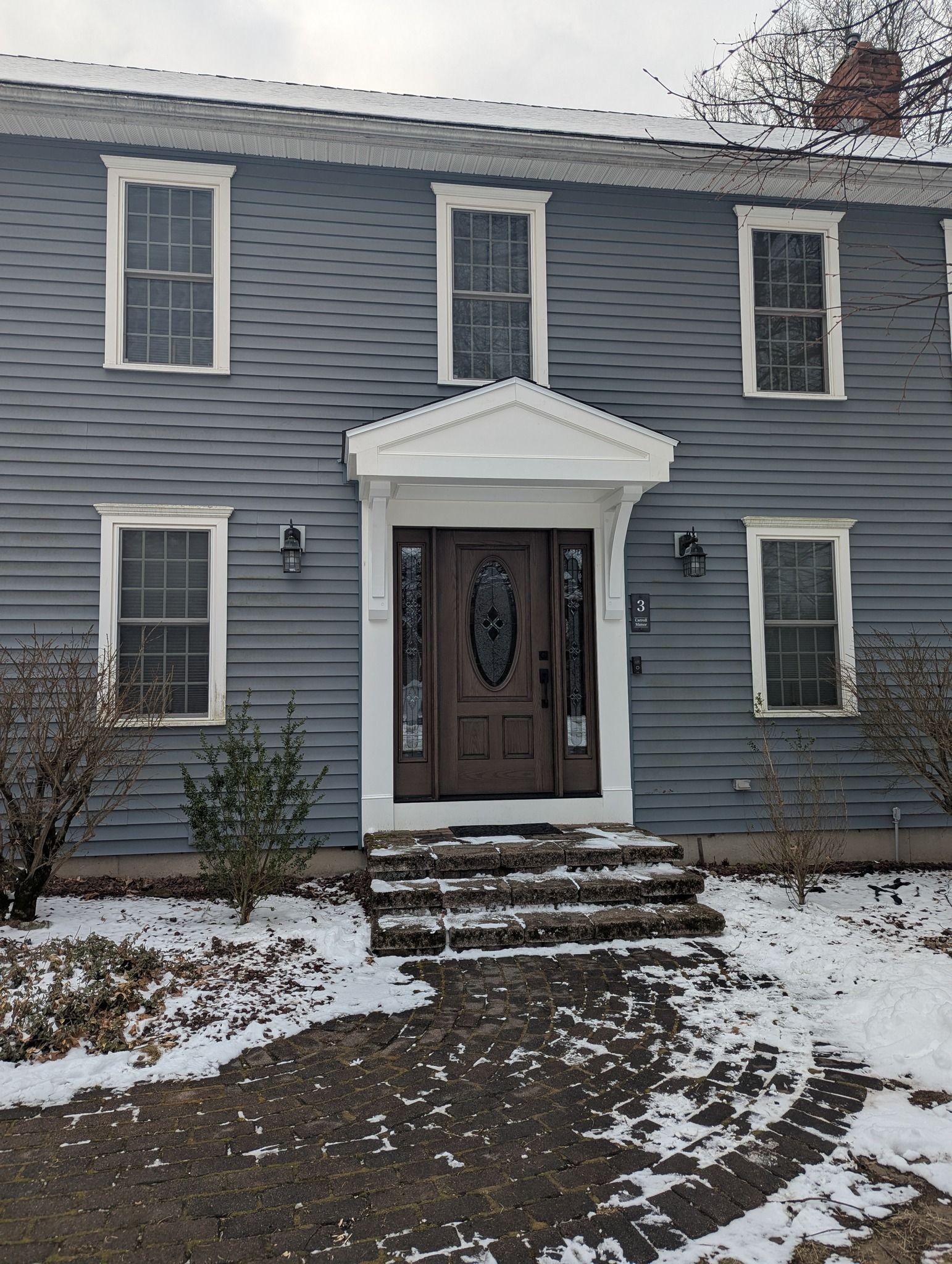 A blue house with a brown door and white trim is covered in snow.