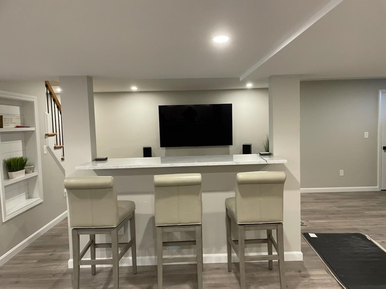 A living room with a bar and stools and a flat screen tv on the wall.