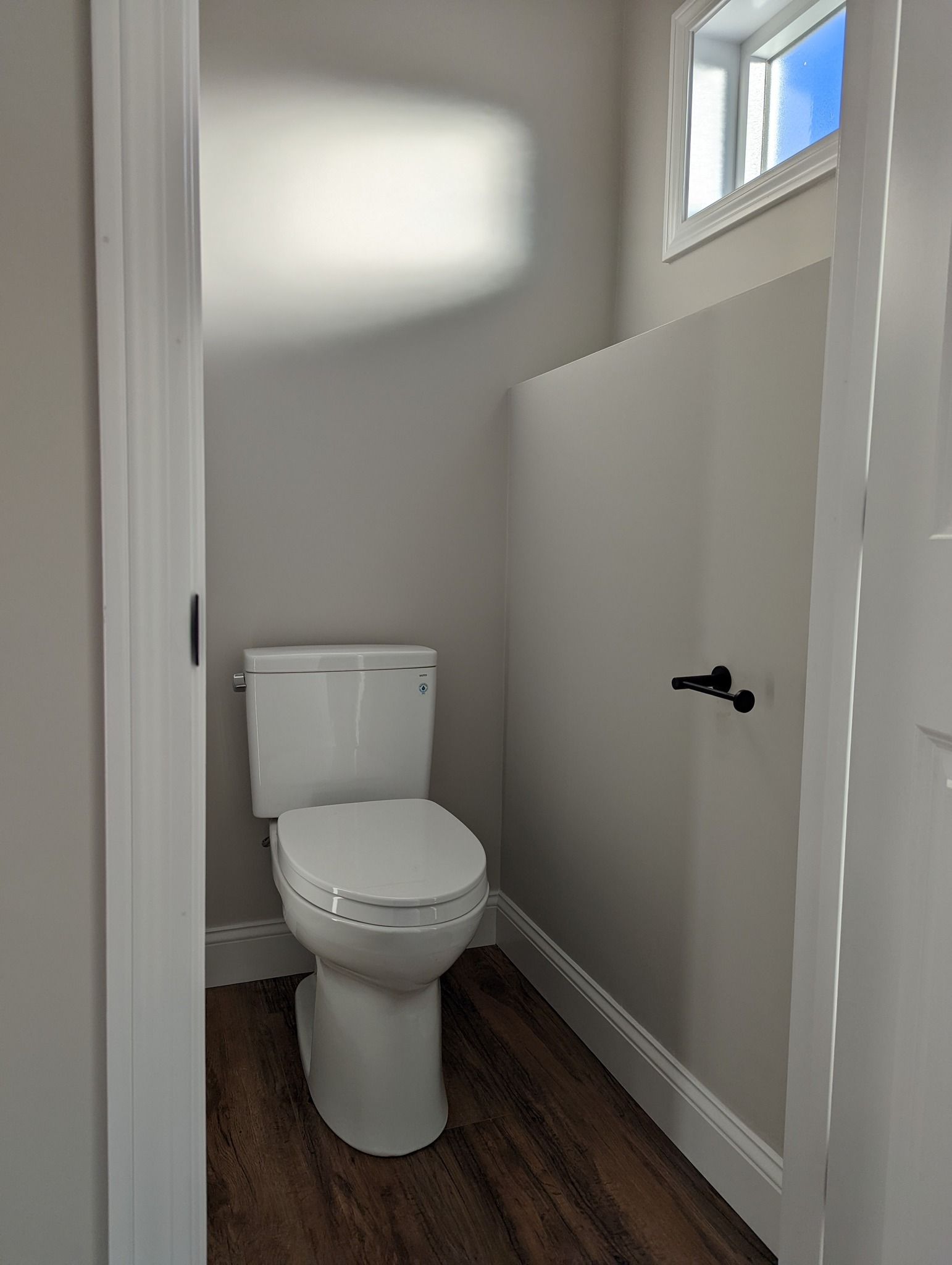 A toilet is sitting in a small bathroom next to a window.