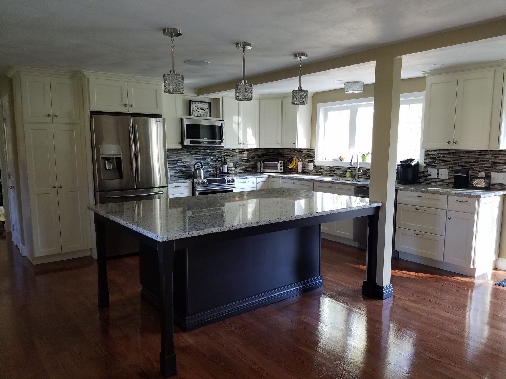 A kitchen with white cabinets, granite countertops, stainless steel appliances and a large island.
