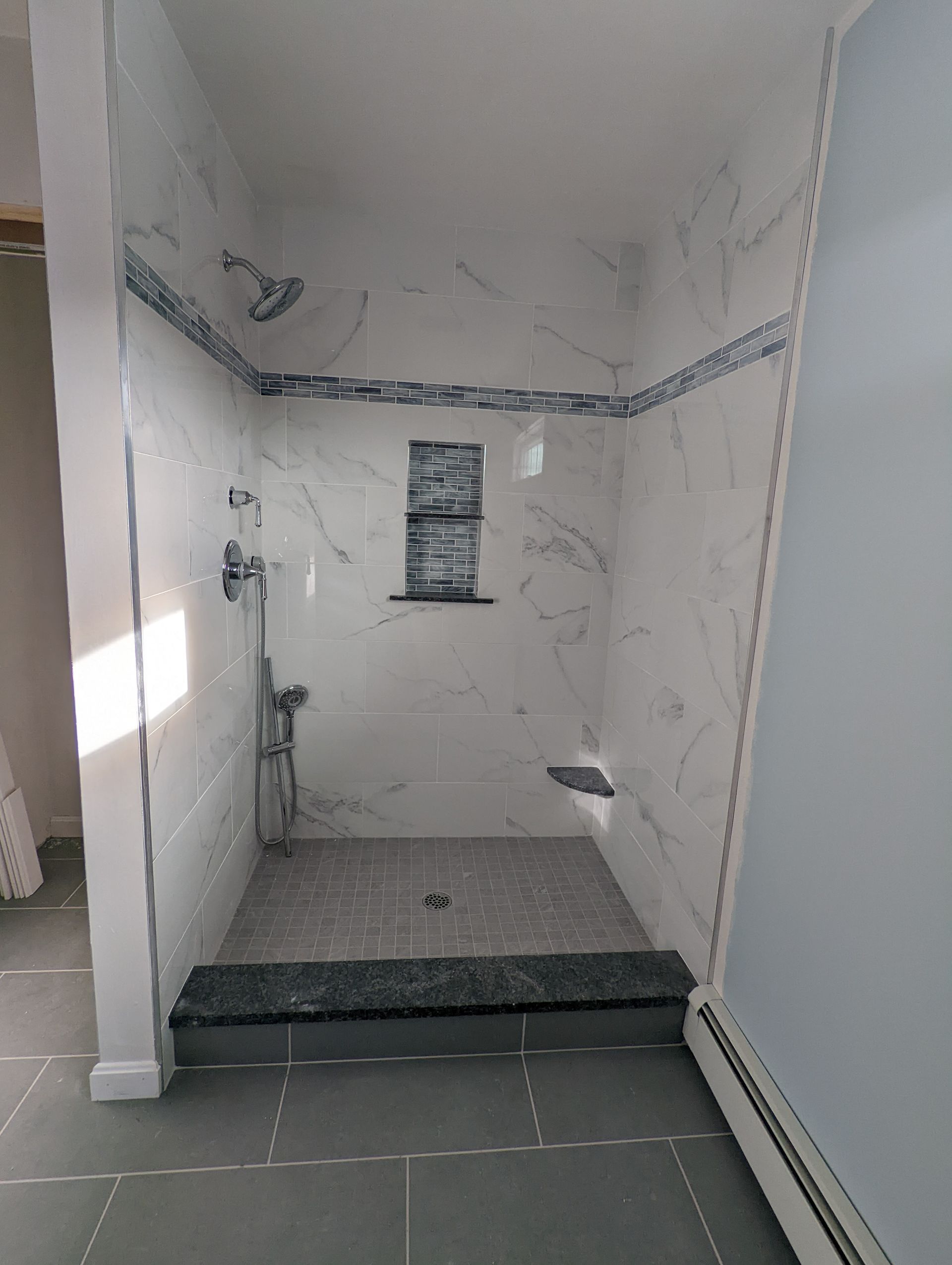 A bathroom with a walk in shower and a marble wall.
