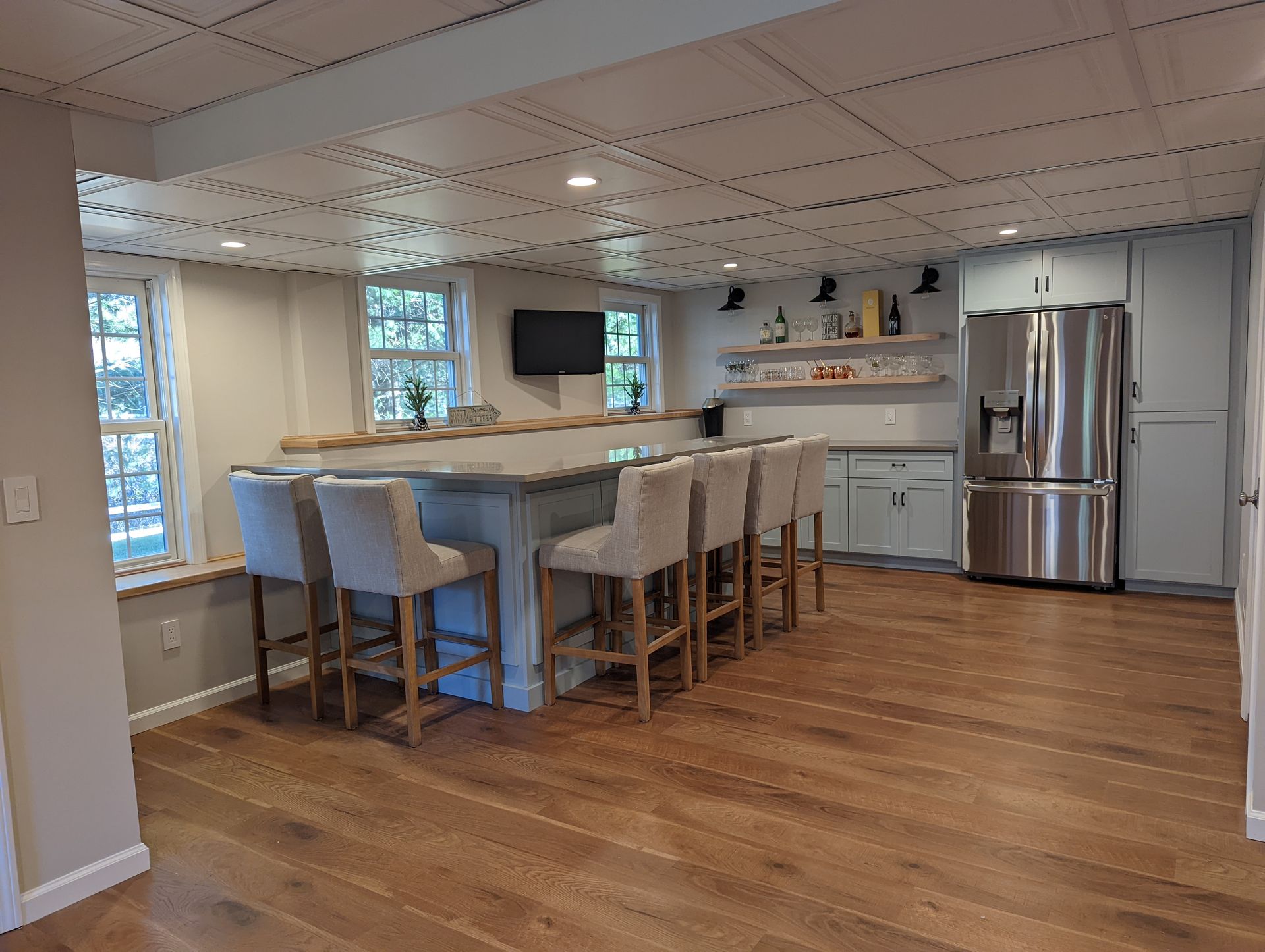 A kitchen with a large island, stools, a refrigerator, and a television.