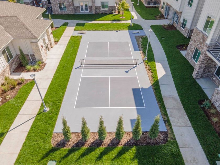 Aerial view of a pickleball court between buildings, surrounded by green grass and sidewalks.