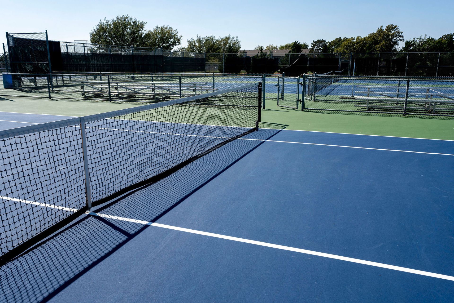Tennis courts, blue and green surfaces, net in foreground, outdoor setting.