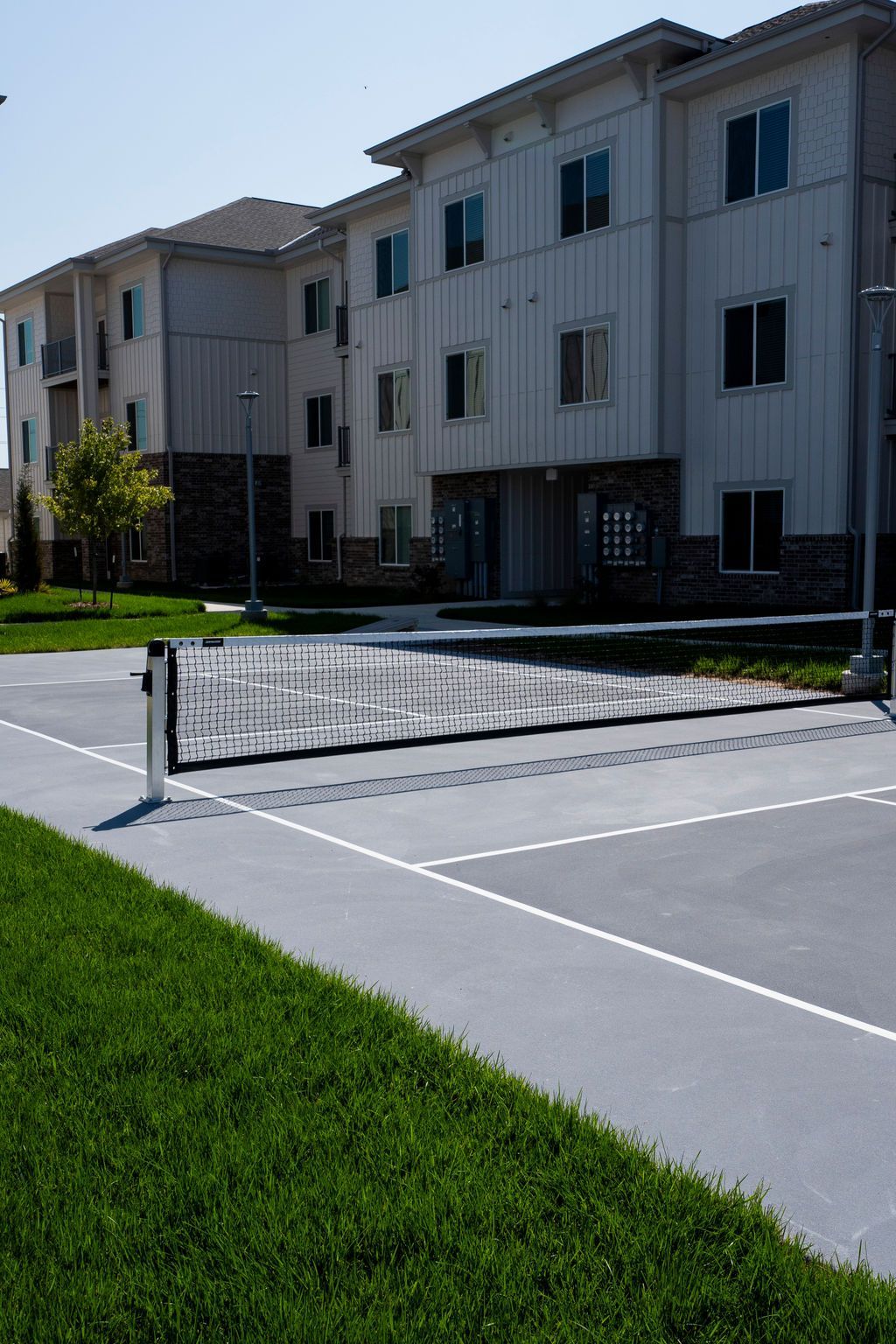 Pickleball court in front of a three-story beige apartment building with green grass.