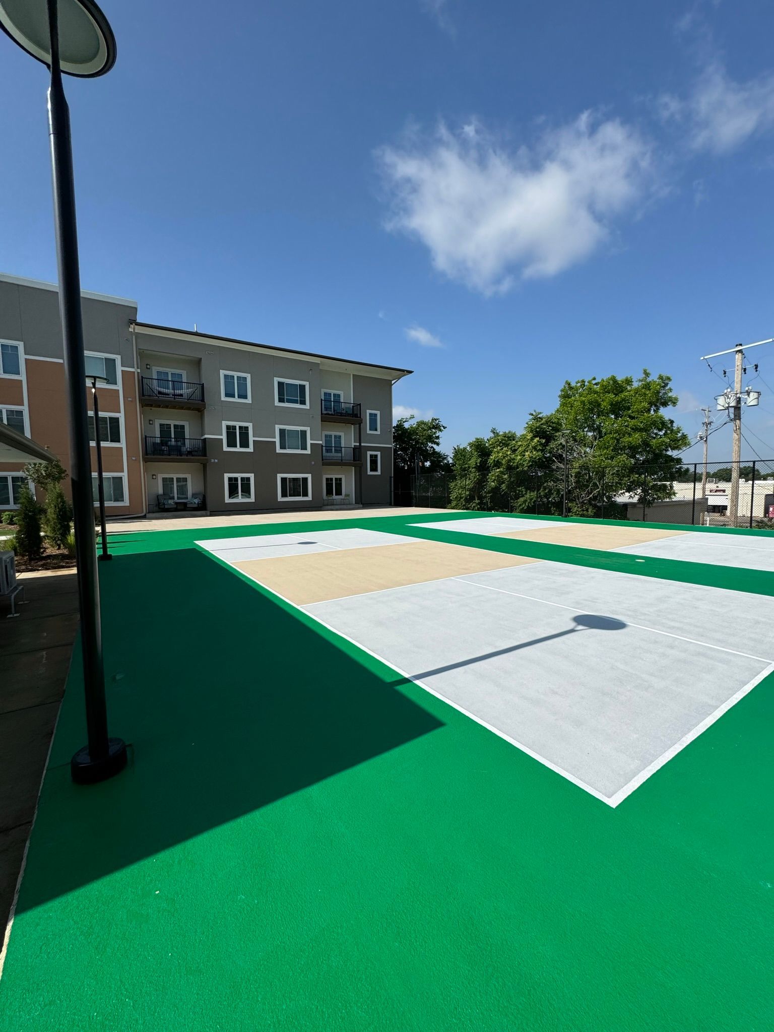 Green and white sports court next to a multi-story apartment building under a blue sky.