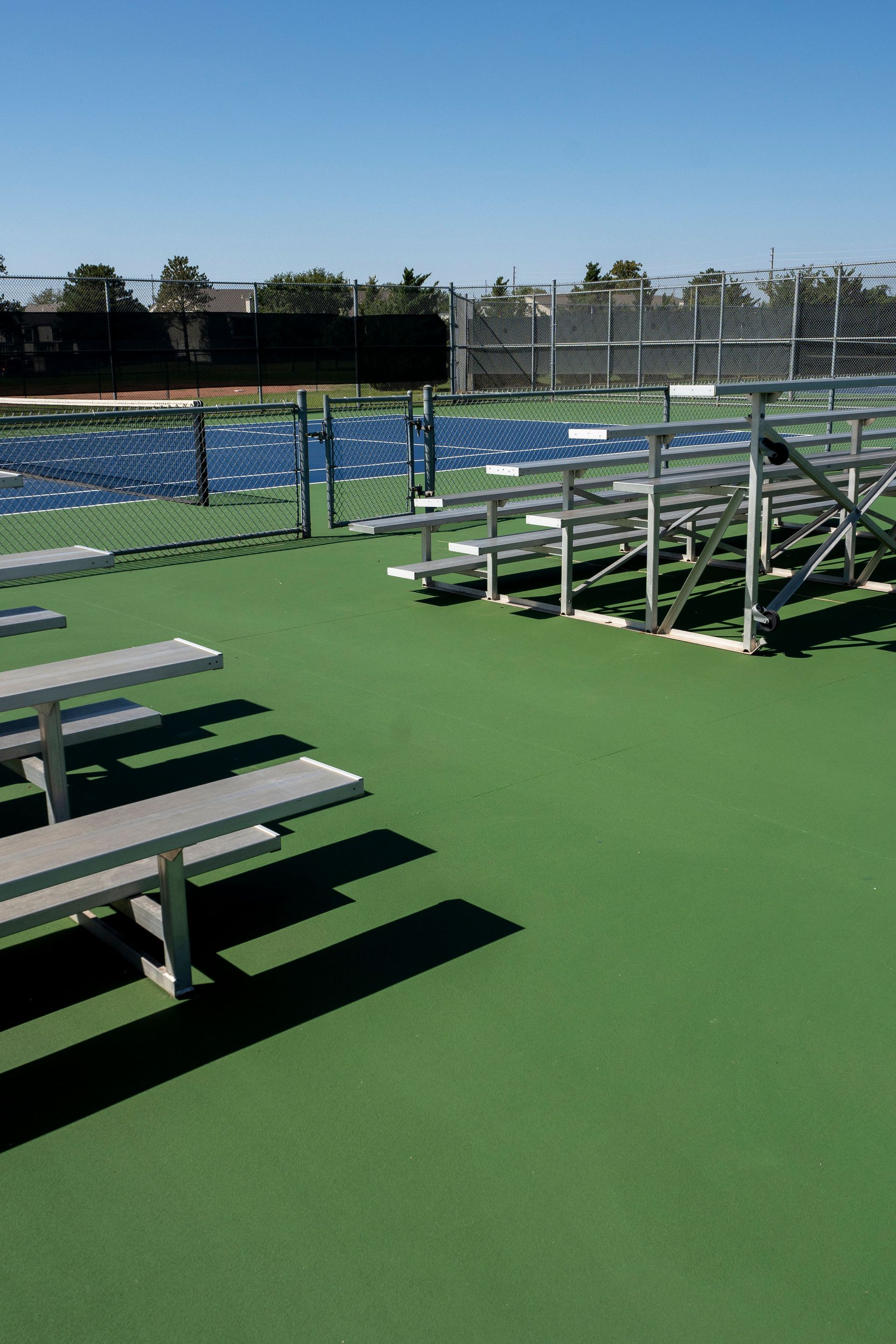 Bleachers overlook a blue tennis court, on a sunny day.