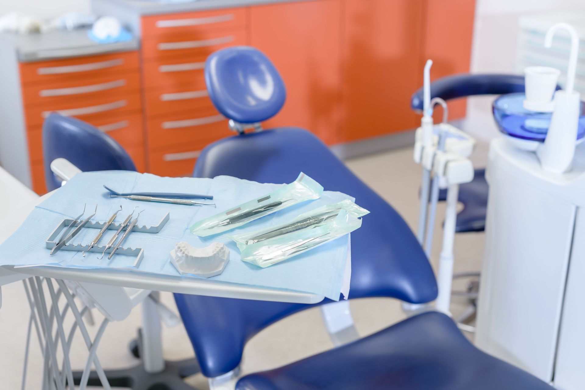 Dental chair with instruments on tray, orange cabinets in background.