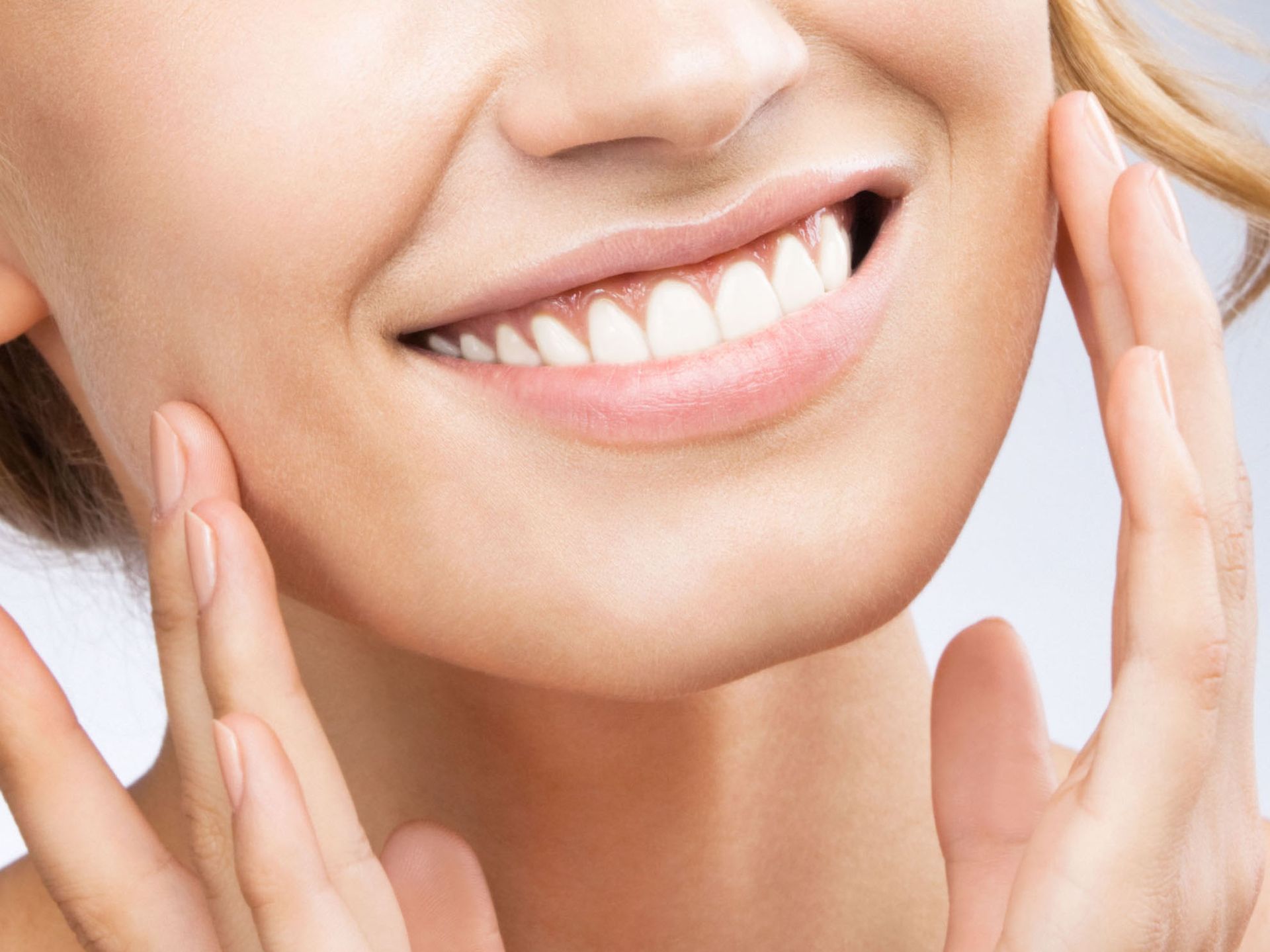Woman smiling with hands on cheeks, showing white teeth.