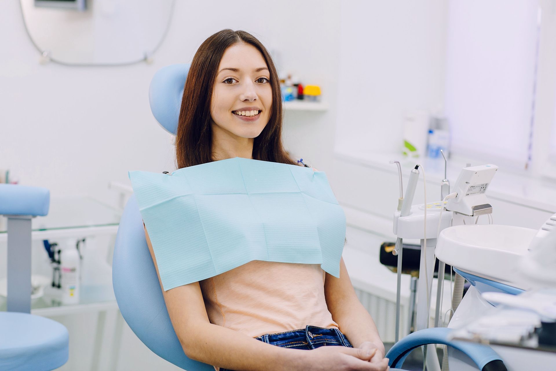 Woman in dental chair, wearing bib, smiling. Dentist office setting.