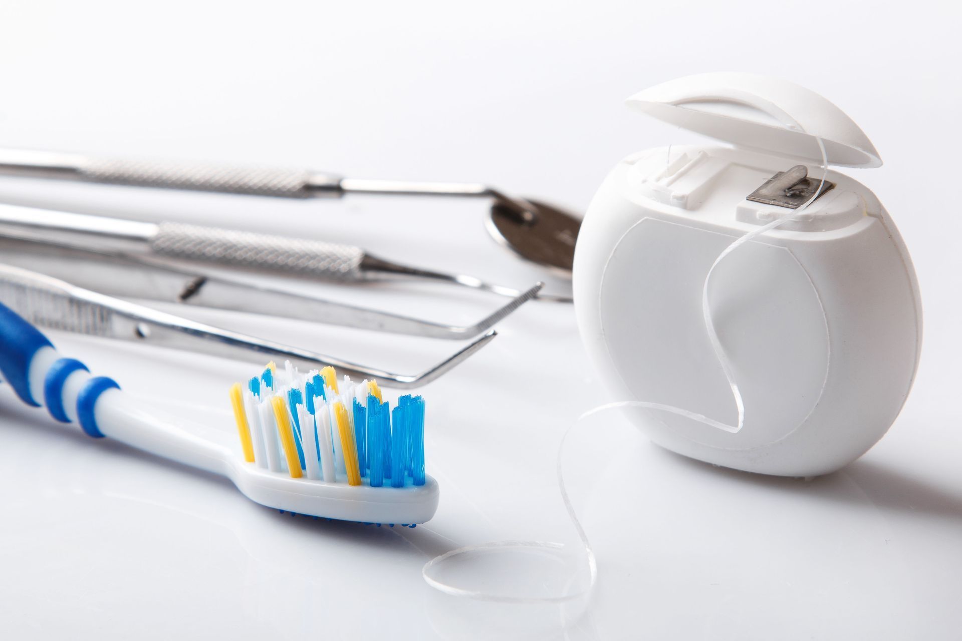 Dental tools, toothbrush, and floss on a white surface.