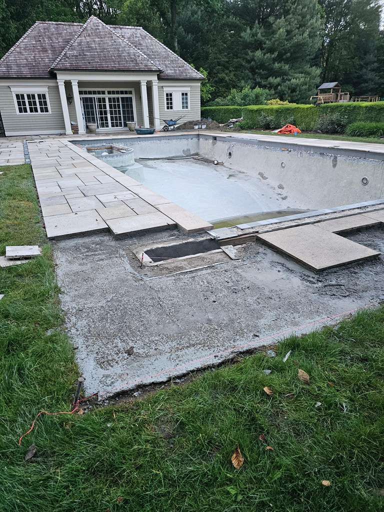 Backyard pool under construction with concrete deck forms beside a house and grassy yard