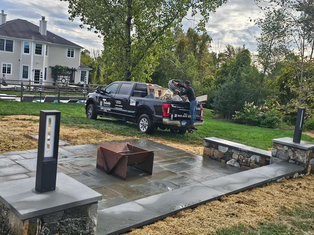 Black pickup truck parked on a muddy lawn beside a stone patio and modern white house.