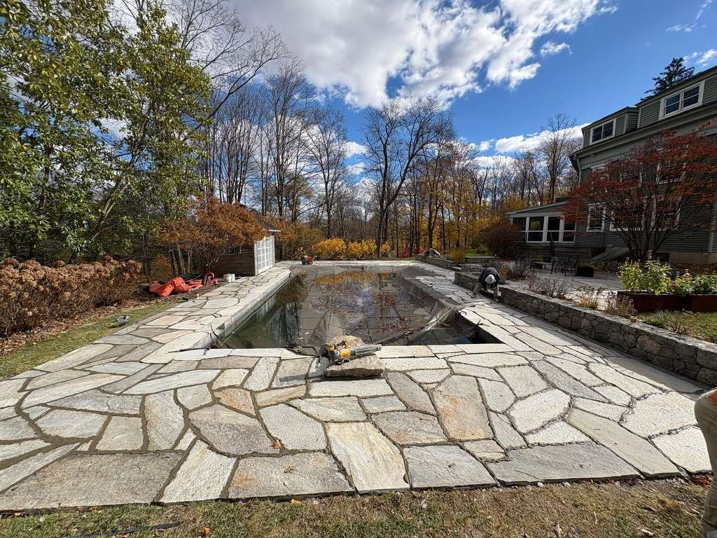 Dry stone-lined empty pool or pond in a courtyard with autumn trees and a building in the background
