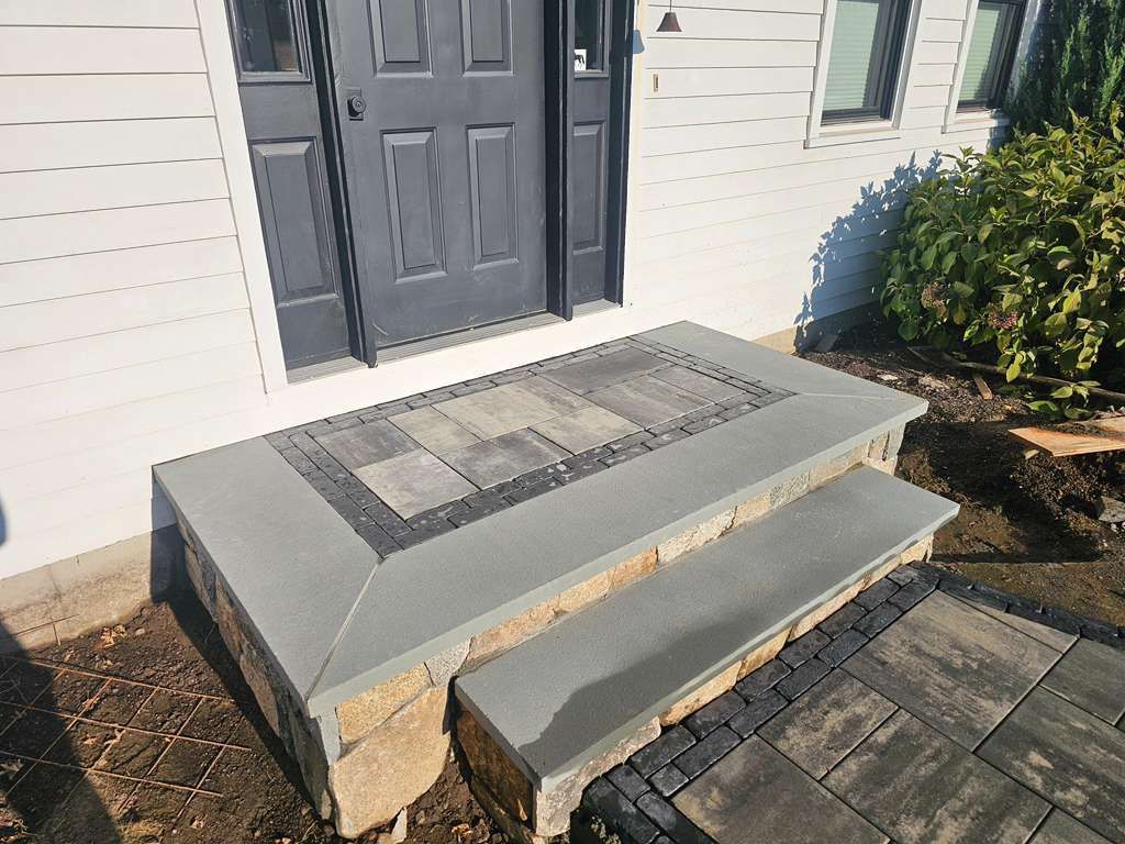 Concrete front steps with a handrail leading to a gray door on a house exterior.