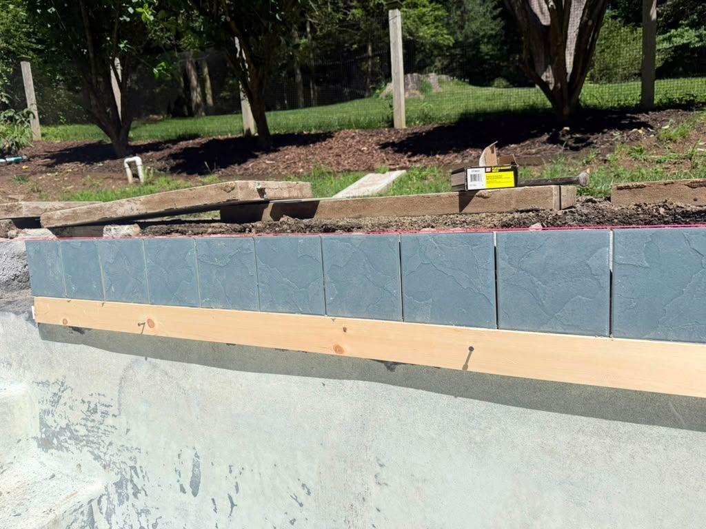 Blue-gray retaining wall with tan trim beside a landscaped outdoor area and trees