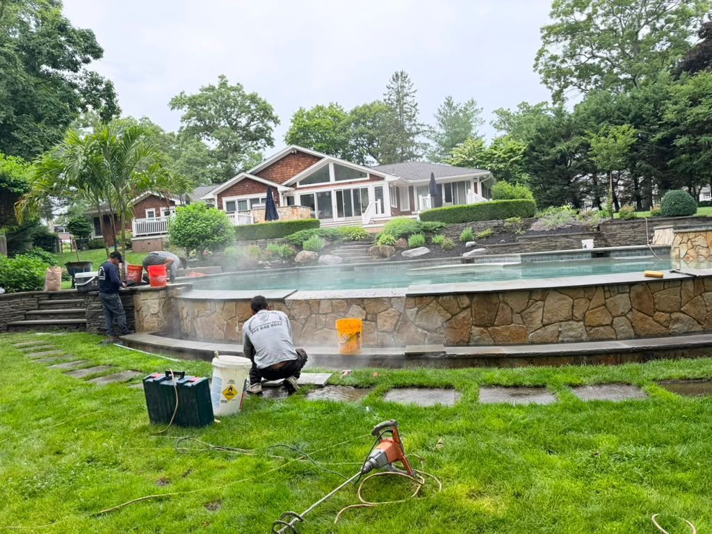 Workers cleaning a large outdoor fountain in front of a house and trees