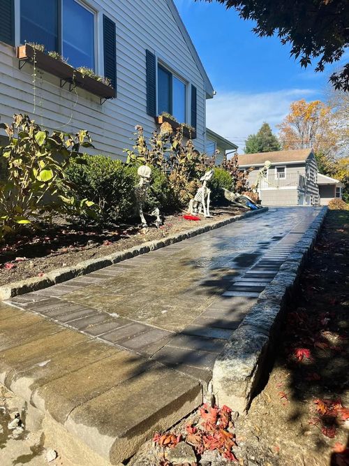 Stone walkway beside a blue house with shrubs, leading to a garage under a clear sky.