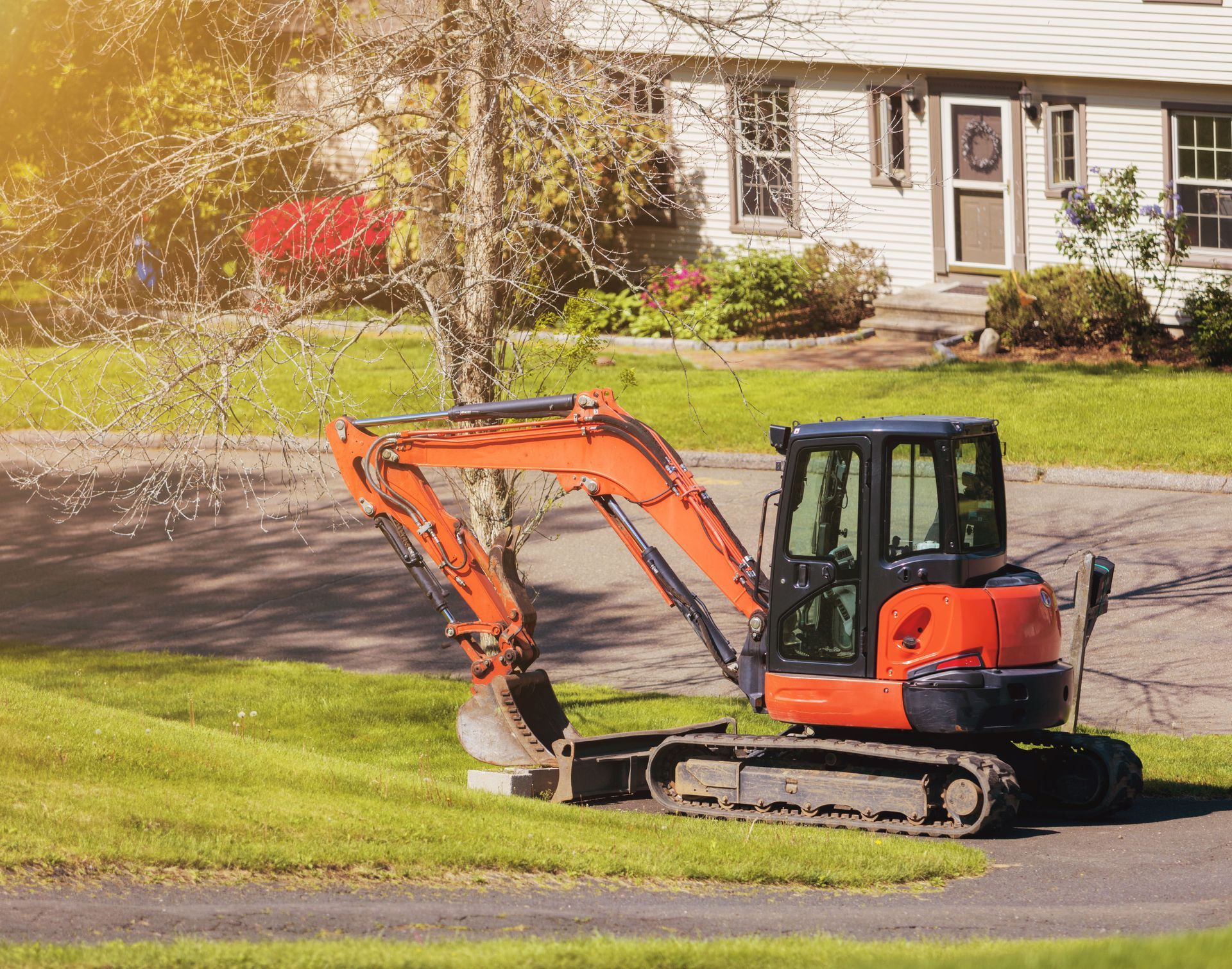 Orange excavator parked on a lawn in front of a house.