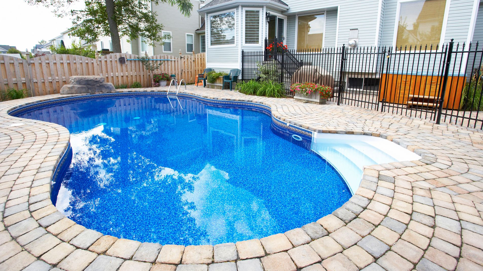 Swimming pool with blue water surrounded by brick patio. White house in the background.