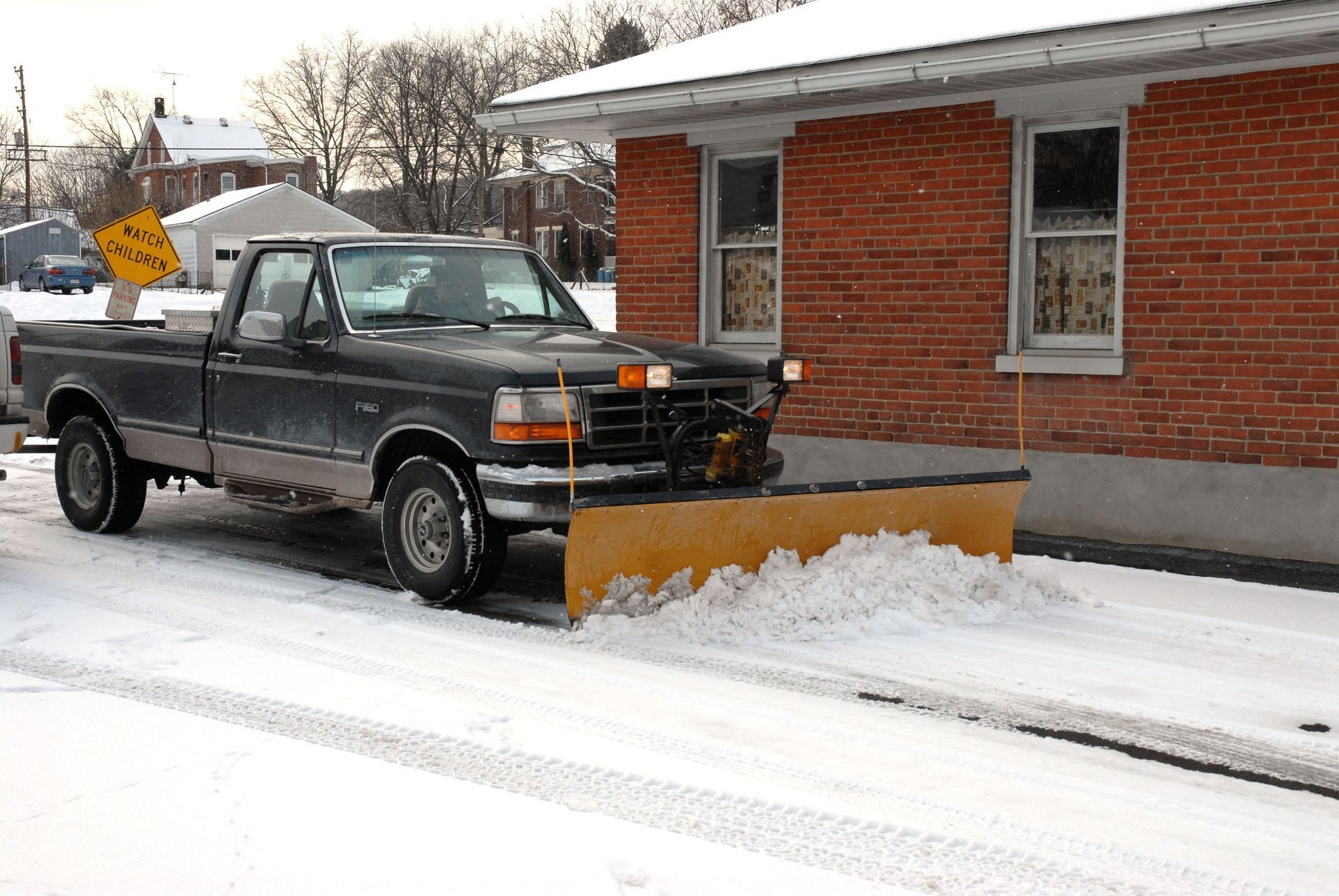 Snowplow truck plowing snow from a street next to a brick building.