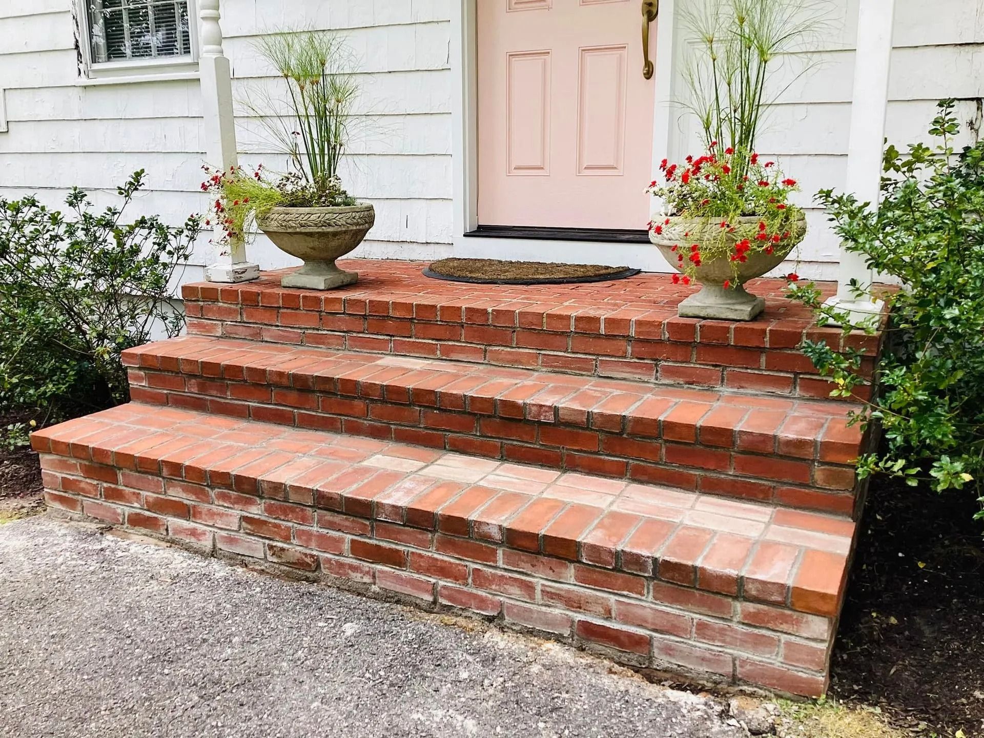 Brick steps leading to a pink door with planters on either side; a close-up exterior view.