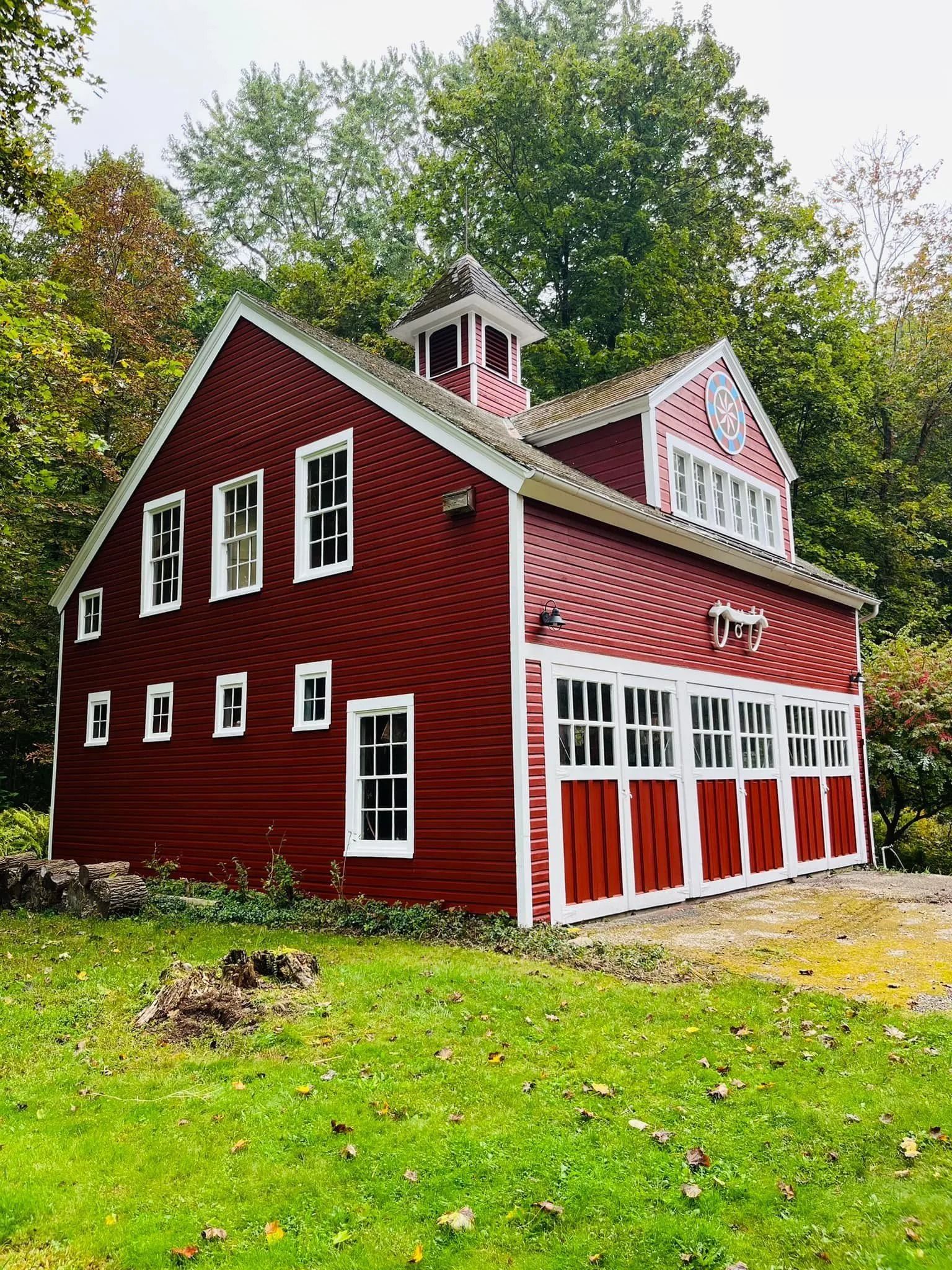 Red barn-like building with white trim, multiple windows, and a cupola; set in a grassy area surrounded by trees.