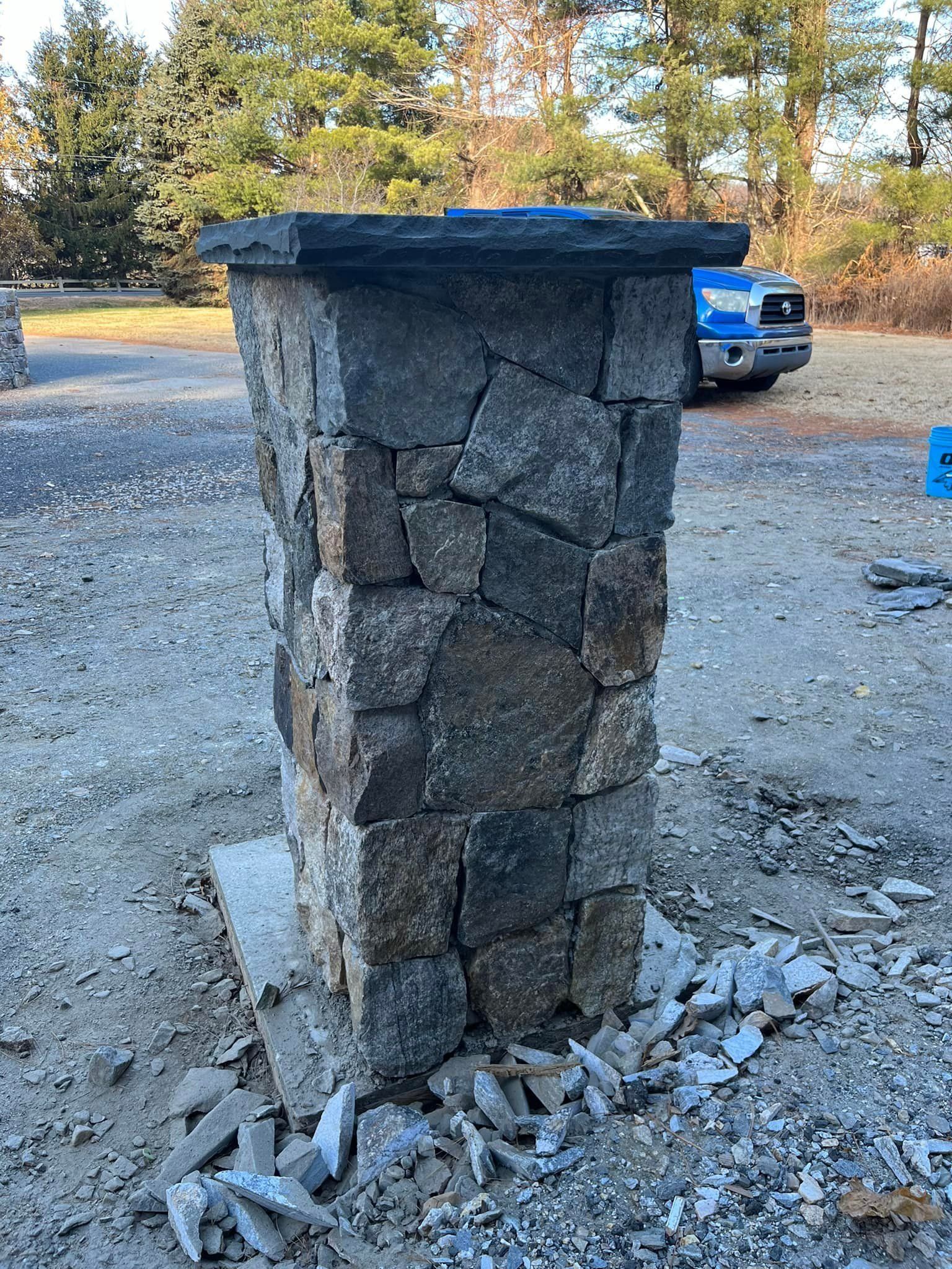 Stone pillar under construction, gray stones with dark top; outdoor setting.