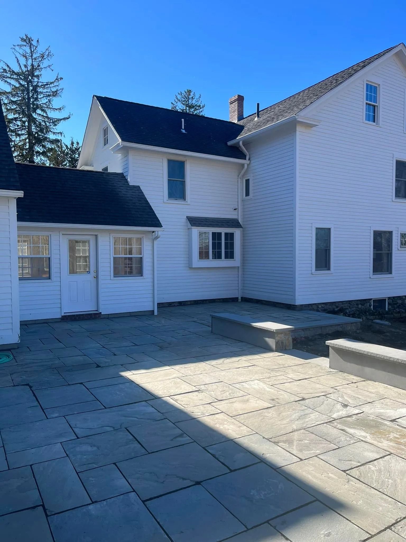 Back of a white house with a new stone patio in the sunlight.