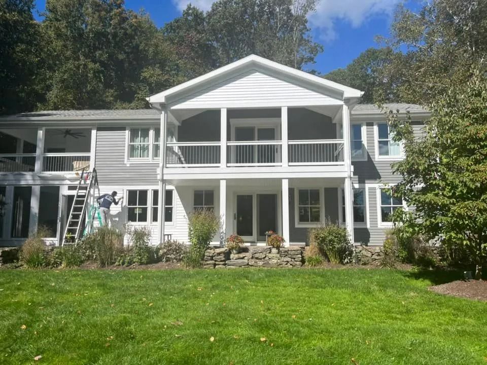 Gray house with white trim, two-story covered porch, green lawn, trees, blue sky.