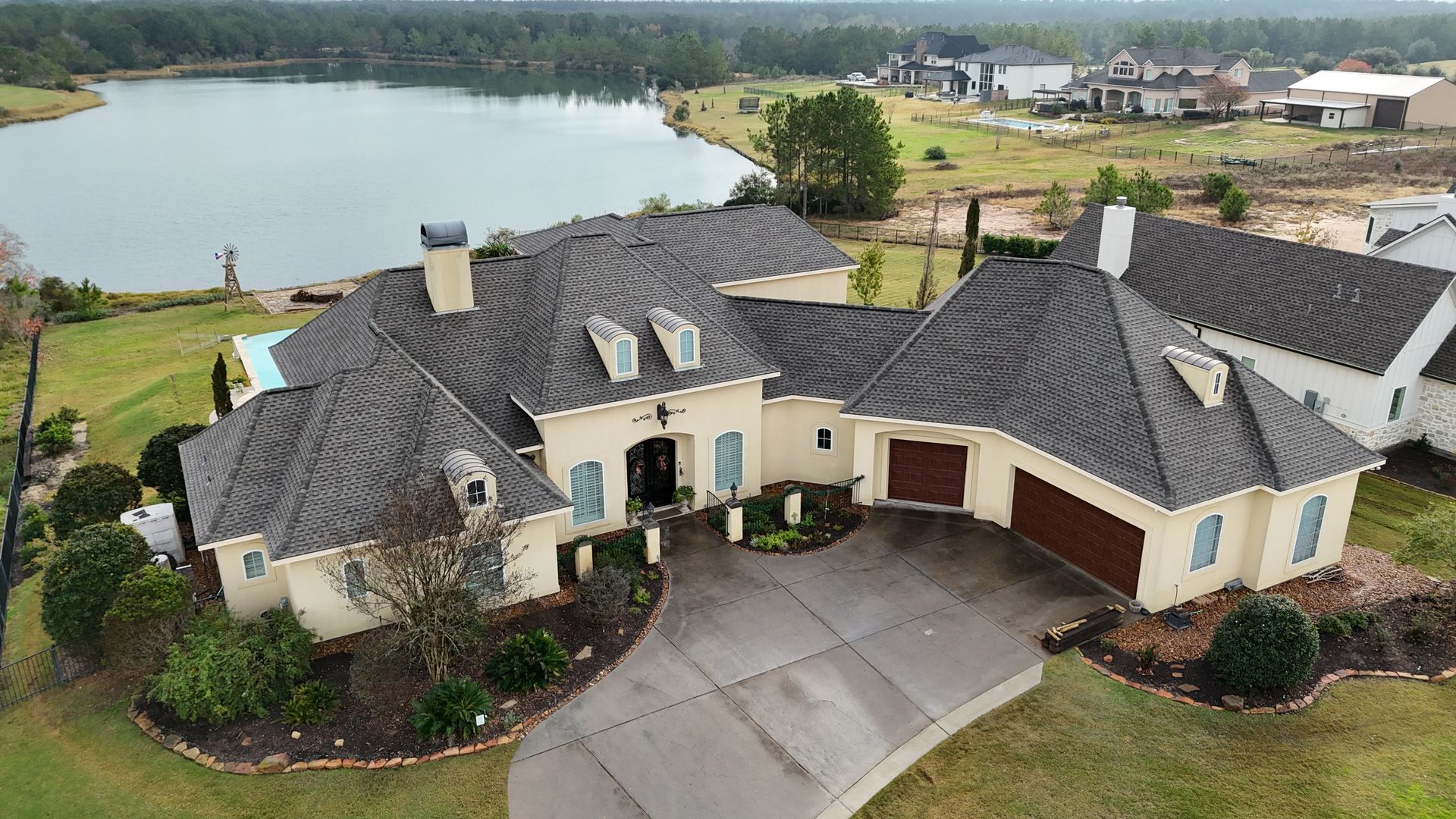 Large house with a lakefront view, gray roof, beige siding, and brown garage doors.